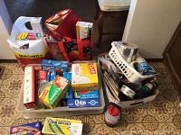 Photo showing assorted kitchen and household boxes and bags containing wraps, bags, batteries, tapes, paint brushes, and other household items arranged on the floor.