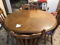 Round wooden dining table with four wooden chairs positioned around it. Table top showing radial wood grain pattern and rounded edge molding.