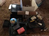 Overall view of office supplies including shredder, printer, metal organizers, desk lamp, globe, and various cords and power strips.