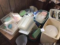 Overview of assorted white and pastel-colored plastic containers, cake holders, jugs, and laundry hampers stacked together.