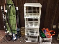 Photo showing the green ironing board, metal drying rack, two irons, steamer, plastic shelving, wicker basket, plastic crate with reusable bags