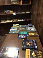 Wide view of table and shelf holding assorted game boxes, rulebooks, manuals, novels