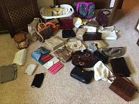 View of assorted purses, wallets, bags, and a laundry basket arranged on a carpeted floor showing variety and quantity.