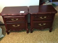 Front view of two matching wooden nightstands showing the curved edges, brass handles, and carved legs.