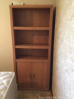 Front view of wooden shelving cabinet with three shelves and two-door storage cabinet below, showing overall condition and details.