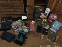 Photo showing assorted scarves, mug, glass duck figurine, decorative plate, camera film, small framed art, gloves, wallets, and small miscellaneous items laid on carpet with wood furniture background