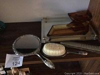 Photo showing vintage hair brush with white bristles, matching hand mirror, metal comb on shelf next to amber colored glass dishes on mirrored tray