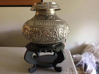 Overall view of silver container on black carved wooden base