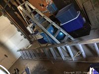 Photo showing both aluminum ladders laid down in garage area with various storage items around them.