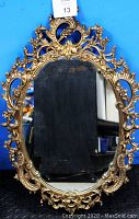 Front view of vintage ornate oval wall mirror showing intricate floral gold-tone frame with some tarnish and aged mirror glass.