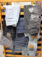 10 pairs of assorted men's and women's denim jeans in different washes and styles arranged on a wooden surface.