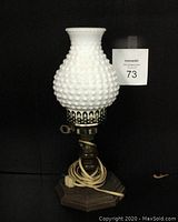 Front full view of vintage milk glass hobnail table lamp, showing the white textured glass shade, brass fixture, wood base with electrical cord.