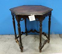 Front view of six-legged dark wood table with octagonal top showing structural legs and connections, surface scratches apparent.