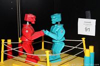 Red and blue classic Rock 'Em Sock 'Em Robots facing each other in yellow boxing ring with white ropes and yellow corner posts.