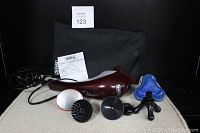 Wide shot showing the maroon and white Wahl electric handheld massager, four different massage attachment heads, black carrying bag, and user manual.