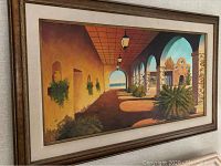 Framed oil painting of a Mexican scene with arches and plants.