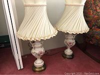 Pair of ornate lamps with cream pleated shades and floral porcelain bases on carpeted floor