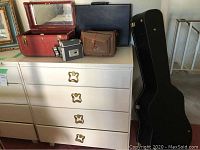 Kodak Cine Video Camera with two lenses, brown camera case, two leather briefcases, black tote bag, and black guitar case positioned beside dresser.