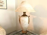 Full view of one ceramic lamp on glass table with beige/tan lampshade, showing overall appearance, color and style.