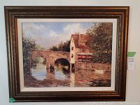 Framed oil painting print showing a stone bridge over a river with a house on the riverbank.