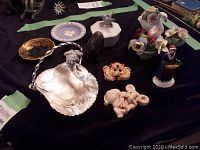 Collection of assorted English decorative items on black cloth including Wedgewood jasperware plate, Staffordshire floral ceramics, Lysander pieces, various figurines, and silver-tone serving dish.