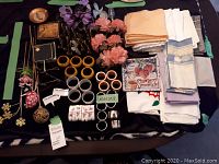 Overview of lot with napkin holders, various folded cloth napkins, faux flowers, small framed art, and assorted decorative items arranged on a table.