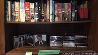 Books on upper wooden shelf, mostly hardcover and paperback, some appear to be fiction or historical titles