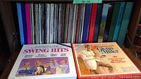 Photo showing a collection of various vinyl albums including 'Swing Hits' and 'The Unforgettable Glen Miller'. Albums are on shelves with visible colorful covers.