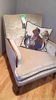 Front and side view of beige crushed velveteen armchair with wood trim and decorative cat pillow on seat.