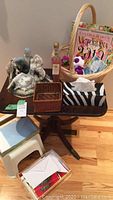 Photo of small wood clawfoot table with porcelain figurine, wicker basket, two boxes of note cards, white step stool, and assorted items on and around the table