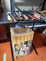 Top view of knives and Oster meat slicer in box on small black folding table