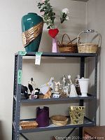 Photo showing a shelving unit with assorted decor items including large green vase, pink vase, baskets, and various figurines.