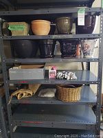 Photo showing multiple garden pots on metal shelving, including terracotta, woven, glazed ceramic, and one large black pot, along with garden gloves and a box.