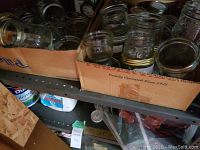 Boxes filled with multiple clear glass mason jars on a metal shelf