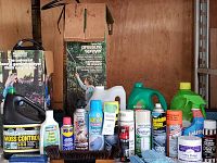 Photo showing assortment of pressure sprayers and multiple cleaning and pest control products arranged on a table against wooden background.