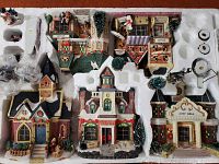 Top-down photo showing multiple porcelain village buildings and village elements neatly arranged in a styrofoam box insert including houses, figures and trees.