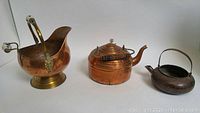 Photo showing three antique copper vessels with aged patina on a white background