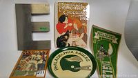 Photo of the sports card, Eagles tray, Eagles pennant, French metal sign, and metal letter E arranged on a surface.