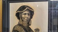 Black and white signed portrait print in black frame with white mat board, showing a person in traditional dress with geometric patterns and tassel earrings holding a staff.