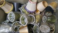 Multiple small lamp shades of assorted colors and styles wrapped in plastic, laid out closely.