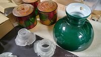 Four stained glass light shades, one large green shade, and four small frosted shades arranged on table with cardboard boxes