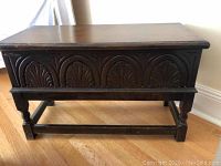 Front view of wooden storage bench showing carved semicircle fan motif on front panel and legs with stretchers.