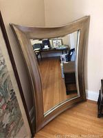 Full view of large beveled mirror leaning against a wall showing its curved rectangular wooden frame and reflective surface.