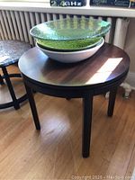 Round wooden side table with three decorative bowls stacked on top, showing table surface and bowls in natural light.