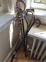 Photo showing a group of canes and an umbrella in a corner, includes wooden canes with curved handles and a cane with a silver dragon handle.