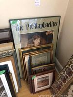 Photo showing several framed prints stacked against a wall including a large print titled 'The Pre-Raphaelites' and several smaller framed artworks.