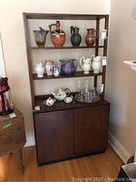 Front view of the cabinet showing open shelves filled with decorative items and closed cabinet below.