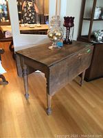 Side view of the wooden drop leaf table showing the drop leaf extension and turned legs.