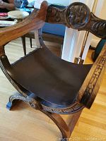 Front angled view showing curved legs, leather seat and carved crest rail