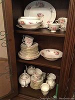 Wide view of coalport china set inside wooden cabinet, showing cups, saucers, plates, serving dishes stacked on three shelves.